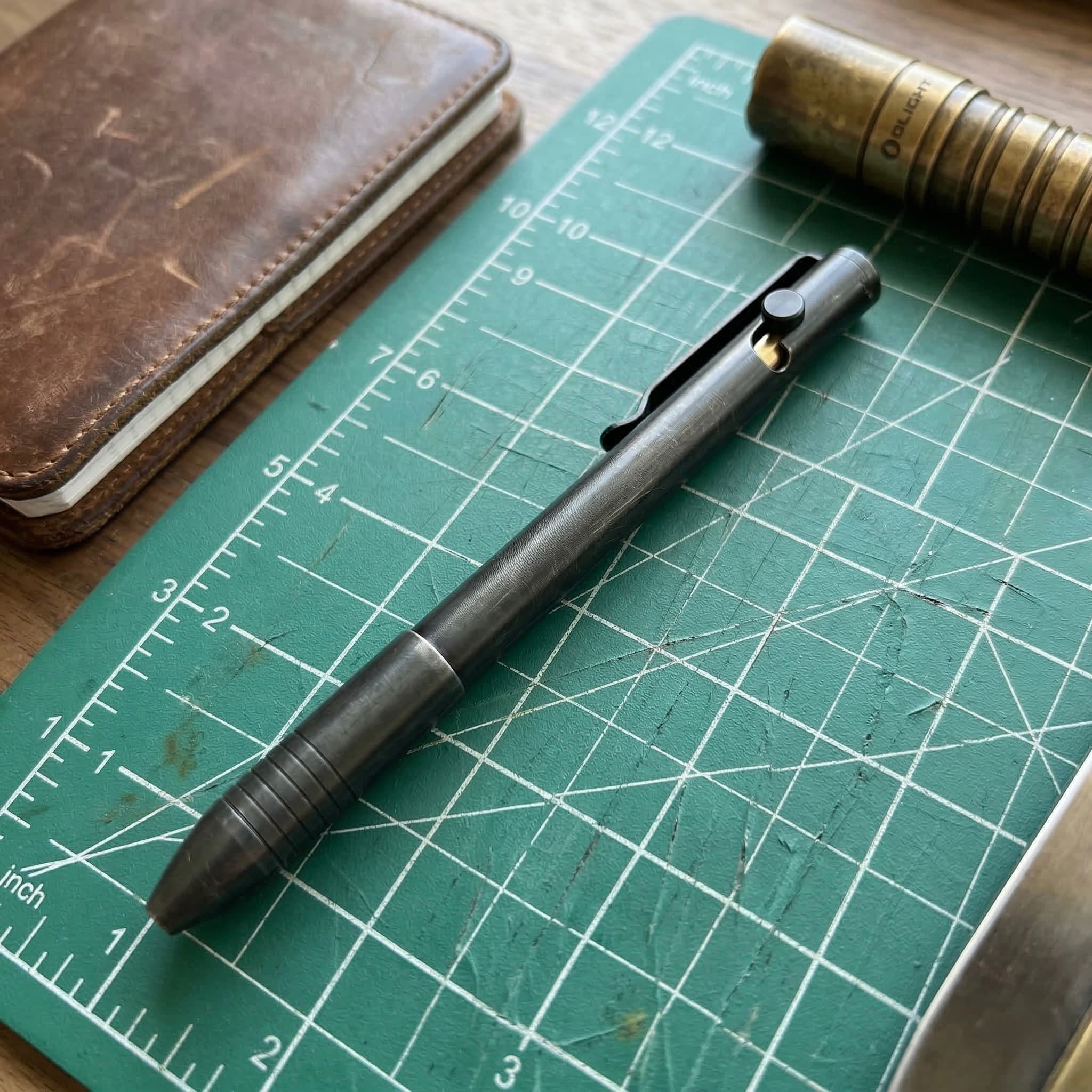 Bolt action pen on a notebook next to a watch
